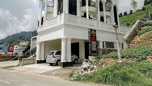 Un bâtiment blanc doté de nombreux balcons et de fenêtres en arc de cercle, une enseigne indiquant « Grand House », et une voiture garée devant.