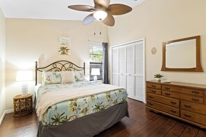 Un dormitorio con cama, lámparas de noche, cómoda, ventilador de techo y ventana con contraventanas.