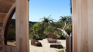 A wooden structure with an arched doorway leading to a garden with various plants and rocks. - Potager House (Carool)
