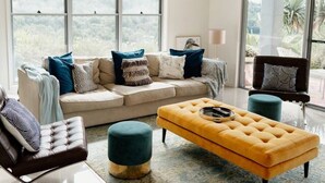 A spacious living room with a large sofa, a yellow ottoman, and a blue armchair. - Potager House (Carool)