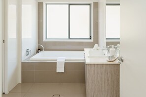 A modern bathroom with a bathtub, a sink, and a window above the bathtub. - Potager House (Carool)