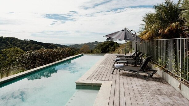 A wooden deck with a swimming pool, lounge chairs, and a view of the surrounding landscape. - Potager House (Carool)