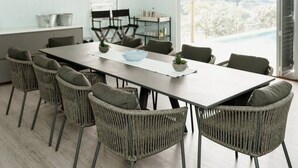 A modern dining area with a long table, wicker chairs, and a ceiling fan. - Potager House (Carool)