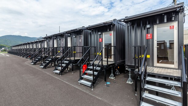 A row of portable cabins with external stairs and a door, each marked with a number. - HOTEL R9 The Yard Tagawakawara (Kawara)