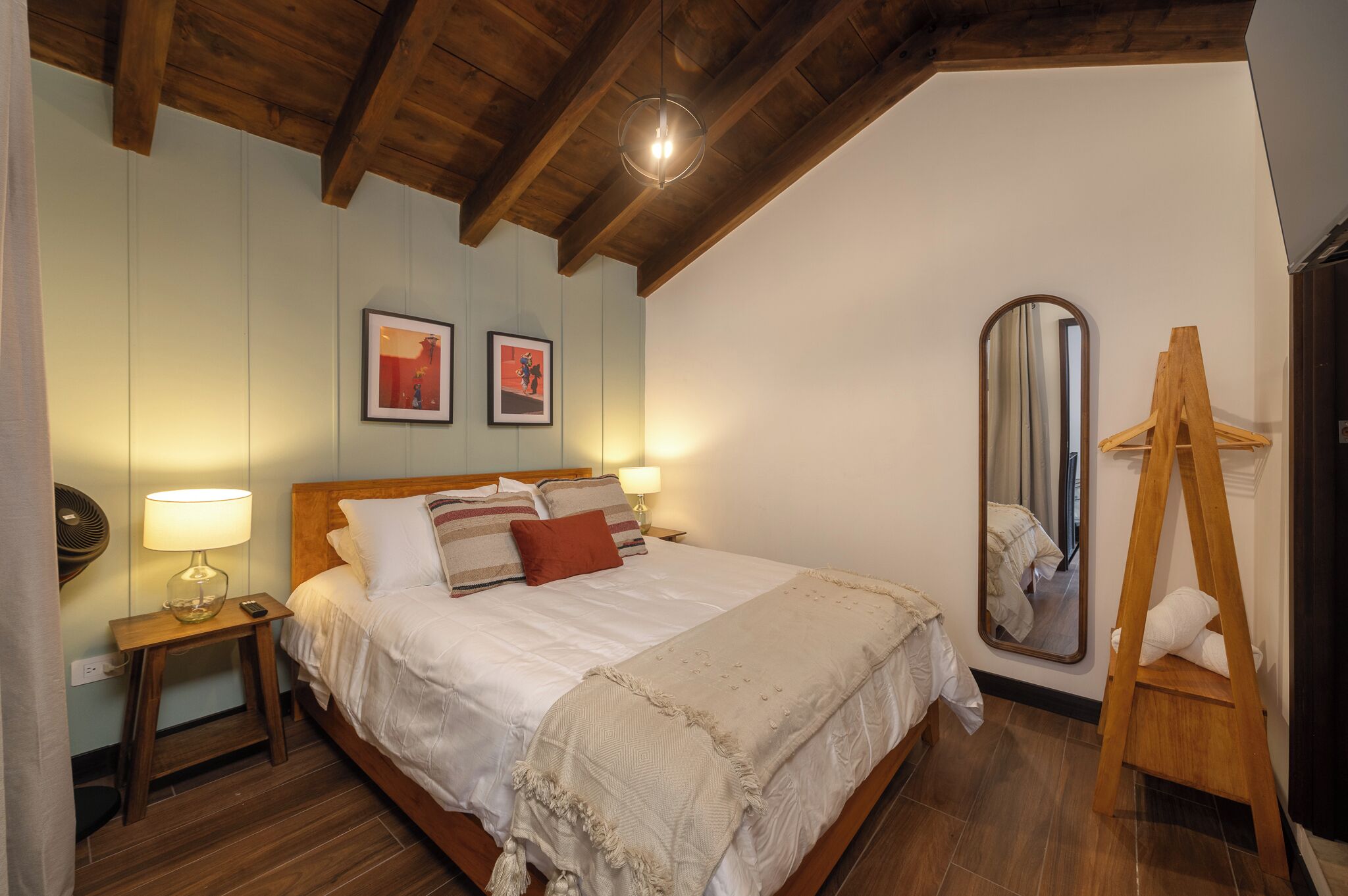 Une chambre avec un plafond en bois, un lit avec une literie blanche, une table de chevet avec une lampe et un miroir sur le mur.