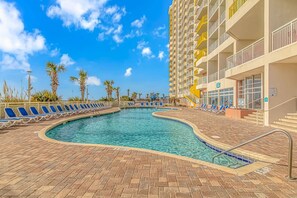 A swimming pool with lounge chairs, a building with balconies, and palm trees. - Bay Watch 706 (North Myrtle Beach)