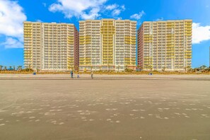 A beachfront high-rise hotel with multiple balconies, a sandy beach in the foreground, and palm trees. - Bay Watch 706 (North Myrtle Beach)