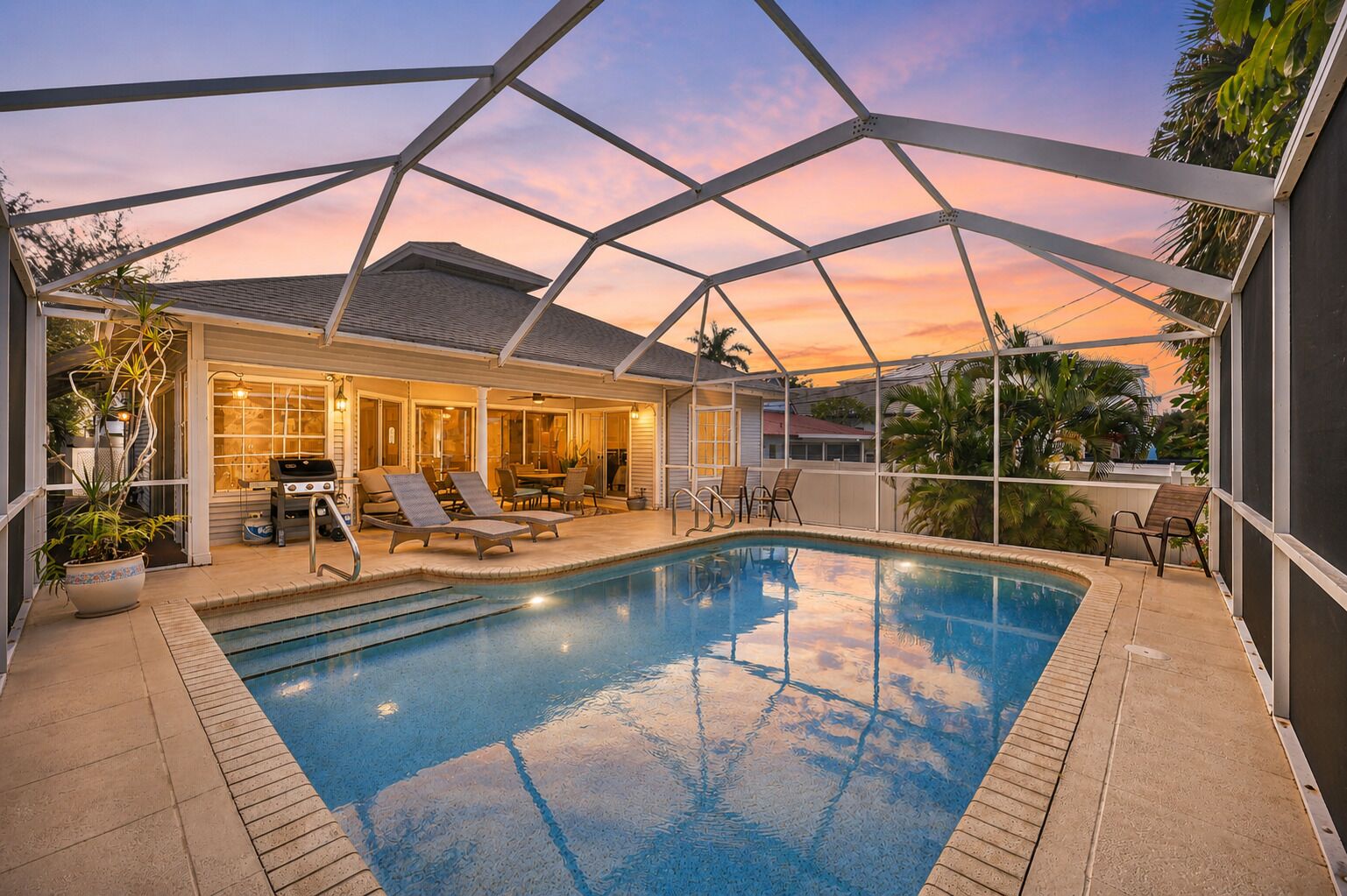An indoor swimming pool with a covered patio area, lounge chairs, and a grill.