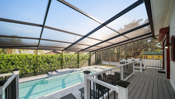 Uma área de piscina descoberta coberta, com vista para a piscina, móveis de deck e uma casa ao fundo.