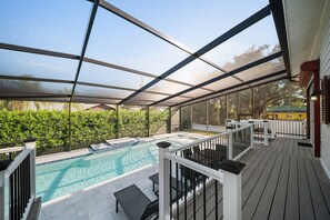 Ein überdachter Poolbereich im Freien mit Blick auf den Pool, Liegemöbel und ein Haus im Hintergrund.