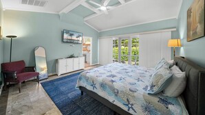 Quarto com cama, uma cadeira vermelha, um armário branco, um espelho grande e uma varanda com vista para o verde.