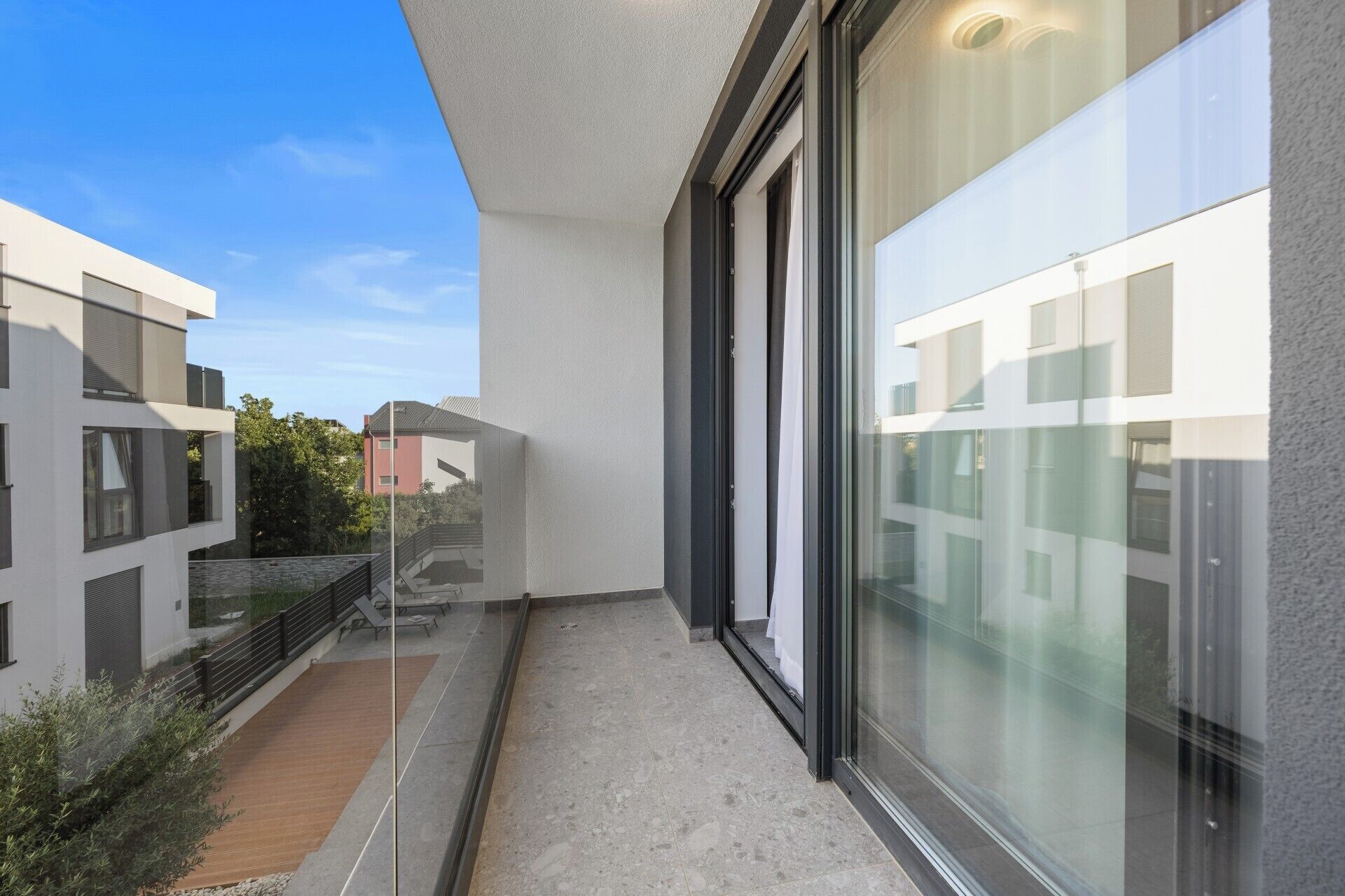 Un bâtiment moderne doté de grandes fenêtres en verre, d’un balcon et offrant une vue sur les immeubles voisins.