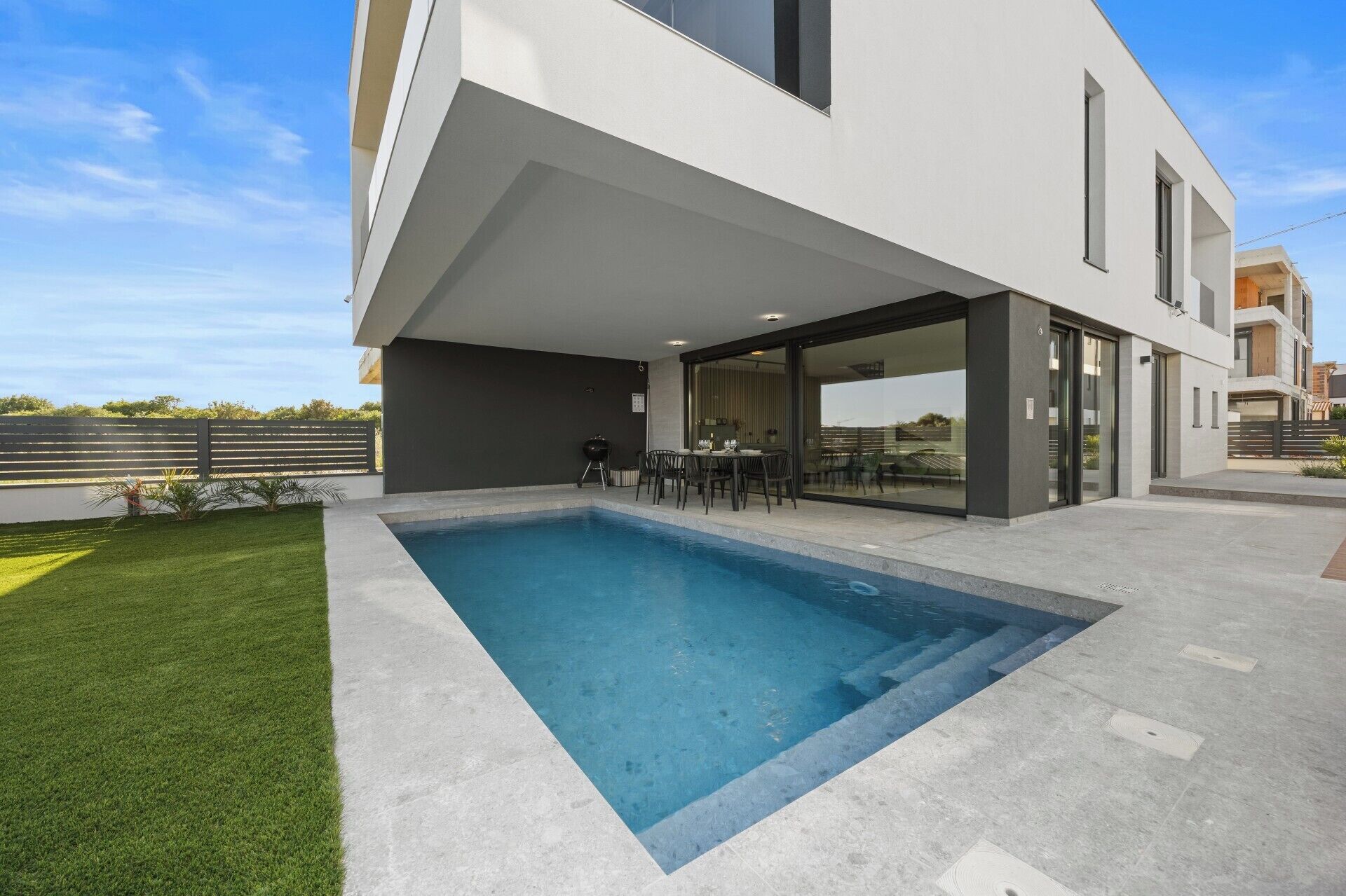 Una casa moderna con piscina, mobiliario exterior y vistas del entorno.