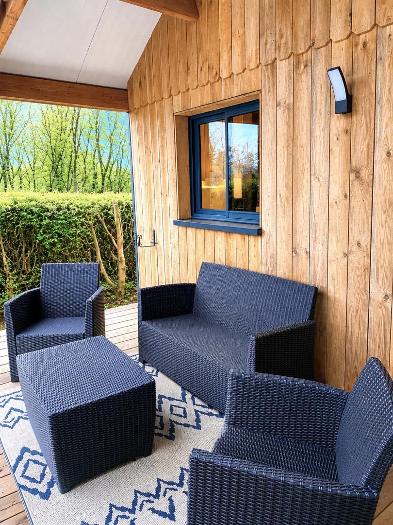 Una terraza de madera con mobiliario de mimbre, una ventana y una lámpara fijada a la pared.