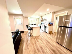 A modern kitchen with a central island, stainless steel appliances, and a seating area with a dark leather couch.