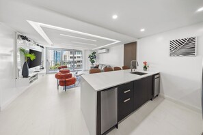 A modern kitchen with a central island, a dining area with red chairs, and a view of the city through large windows. - Beachfront King Suite • Pool • Parking• Walk2Eat (Carolina)