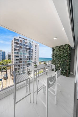 A balcony with a white table and chairs, a view of the ocean, and a building in the background. - Beachfront King Suite • Pool • Parking• Walk2Eat (Carolina)