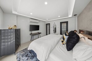 A modern bedroom with a bed, a desk, a television, and a wardrobe. - Beachfront King Suite • Pool • Parking• Walk2Eat (Carolina)