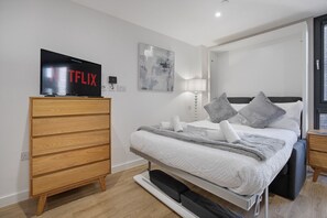A modern bedroom with a bed, a wooden dresser, a TV, and a painting on the wall. - The Point 922 - Grampian Lettings (Aberdeen)