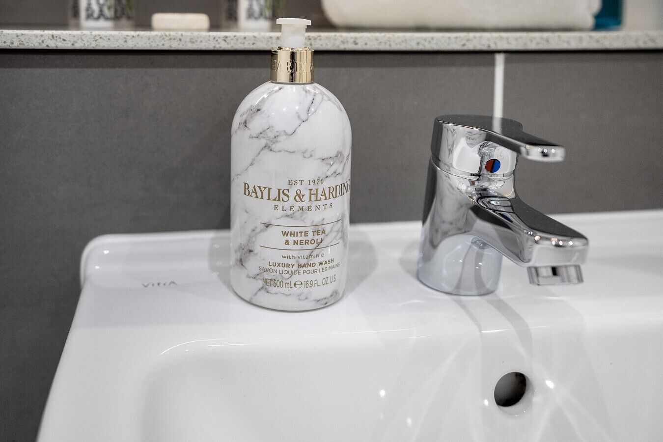 A bathroom sink with a marble bottle of Baylis & Harding Elements White Tea & Neroli, a chrome faucet, and a soap dispenser.