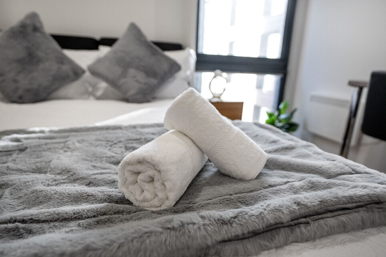 Ein ordentlich bezogenes Bett mit einer grauen Decke und zwei aufgerollten weißen Handtüchern.