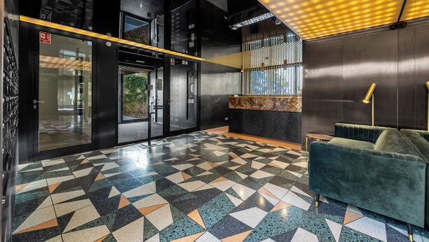 Una hall moderna con un pavimento a motivi geometrici, una scrivania della reception e un divano verde.