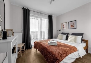 Ein modernes Hotelzimmer mit einem Bett, Nachttischen, einem Schreibtisch und einem mit Vorhängen drapierten Fenster.