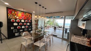 Uma cozinha moderna com uma ilha central, cadeiras brancas, uma seleção de frutas e vista para o mar.