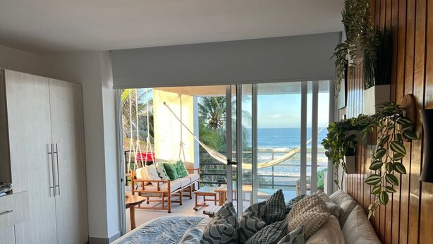 A bedroom with a large bed, a view of the ocean, a hammock, and a balcony with plants.