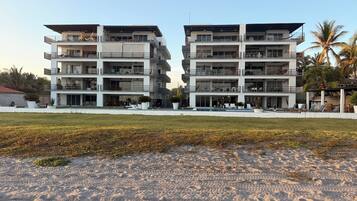 A modern hotel with multiple balconies, a swimming pool, and a beach view.