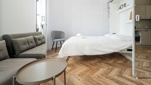 A modern hotel room with a sofa, a small table, a bed, and a view of the kitchen. - Nawrot Modern Apartment (Łódź)