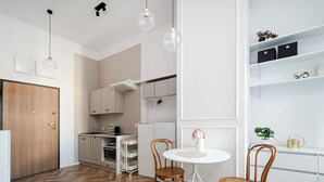 A modern kitchen with wooden flooring, white cabinets, and a dining area with two wooden chairs and a small table. - Nawrot Modern Apartment (Łódź)