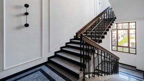 A modern staircase with a wooden handrail and black metal balusters, leading to a balcony with a view of a courtyard. - Nawrot Modern Apartment (Łódź)