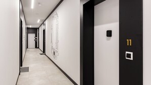En moderne gang med sort-hvid farveskema, med en dør med nummer 11, en vægmonteret lampe og dekorativ vægkunst.