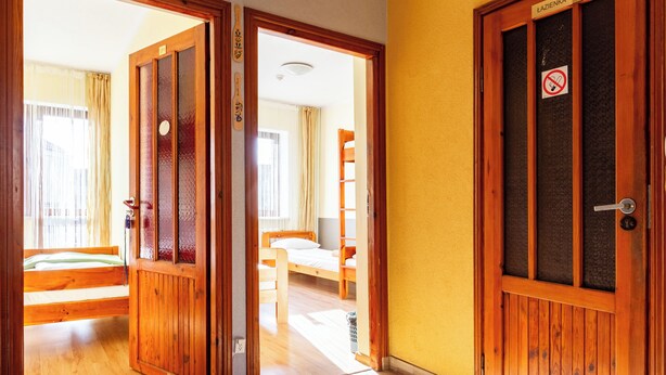 Habitació d'hotel amb portes de fusta, un llit, una cadira i una finestra amb cortines.
