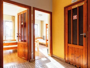 A hotel room with wooden doors, a bed, a chair, and a window with curtains. - Płowce 62 Guest Spot 1P3 (Gdańsk)
