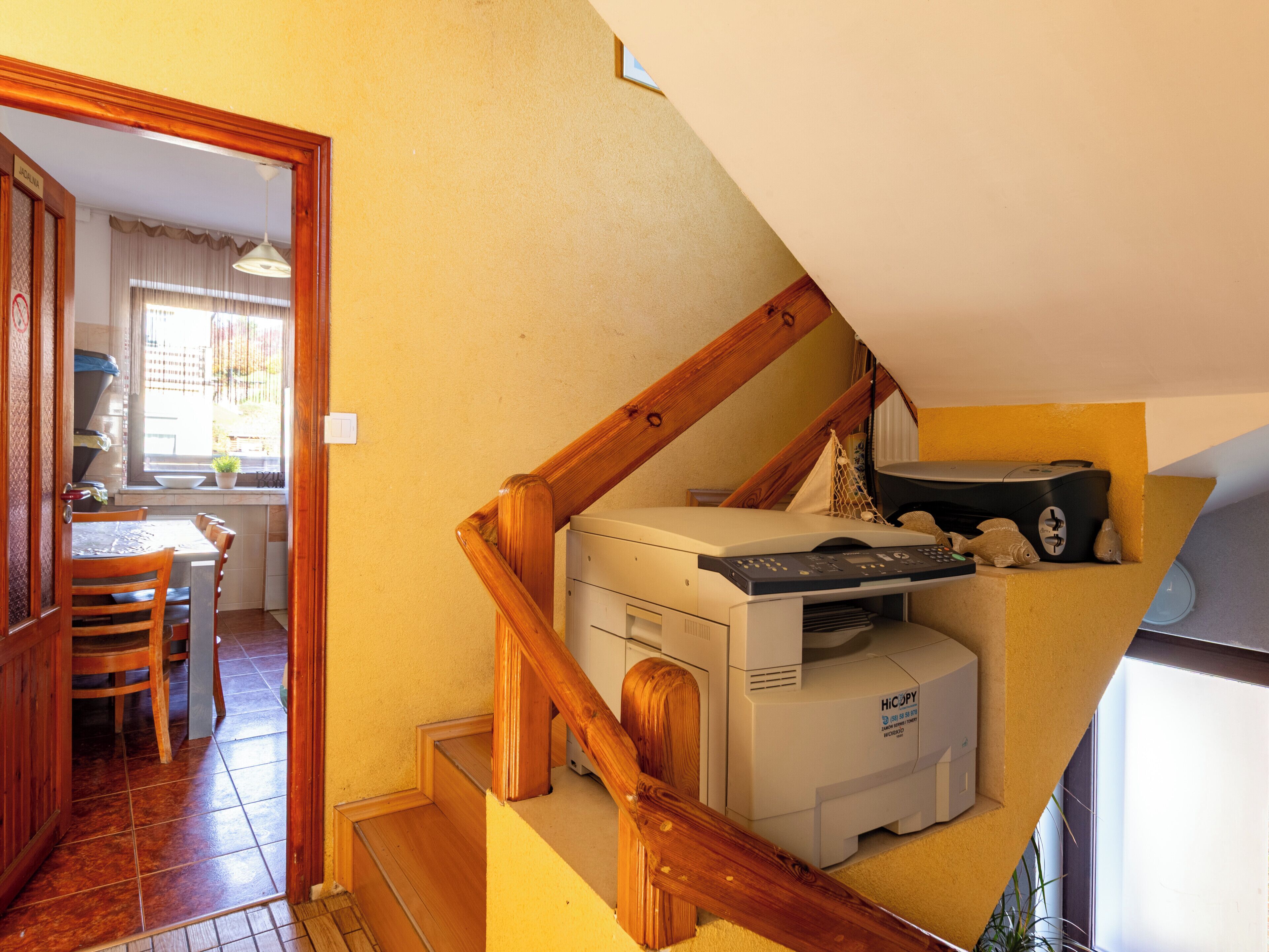A staircase with a wooden handrail leading to a room with a printer and a bed.