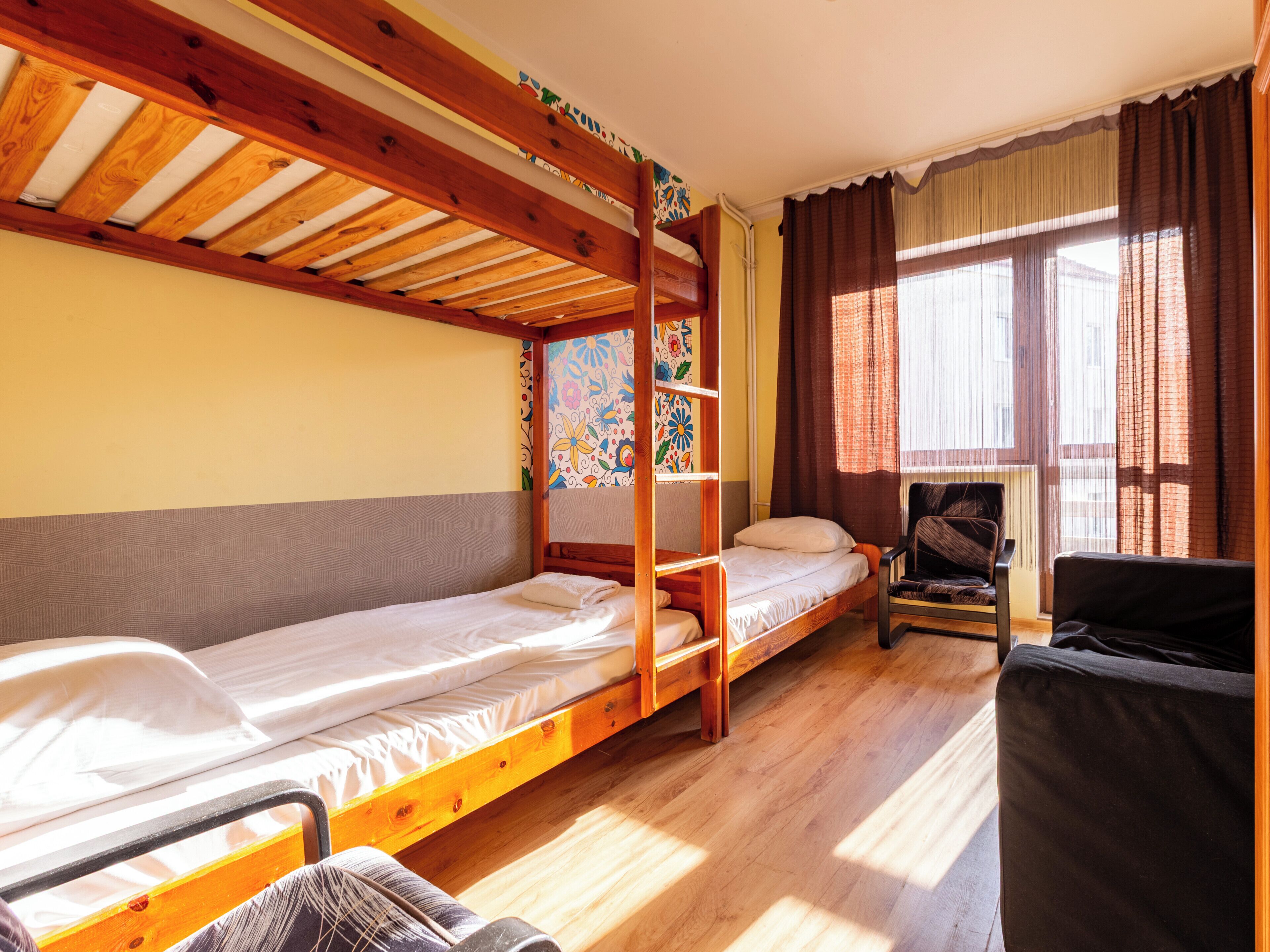 A room with two wooden bunk beds, a chair, and a window with curtains.