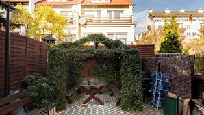 Un pati amb taula i bancs de fusta, envoltat d'una tanca de fusta i cobert d'hedera.