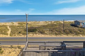 A beach view with a wooden deck, a small building, and a road in the foreground. - Babe's Place | 105 ft to the beach | Dog Friendly (Kill Devil Hills)
