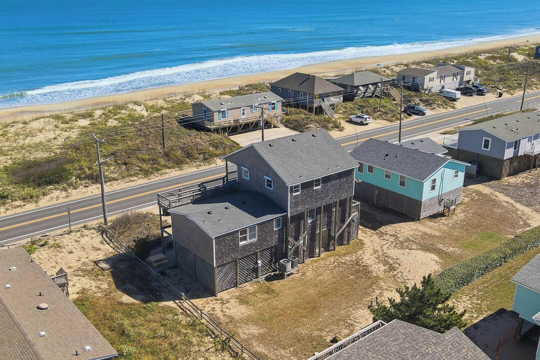 Ett bostadsområde vid kusten med hus nära stranden, en väg och fri utsikt över havet.