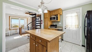 A kitchen with wooden cabinets, a central island, a microwave, and a refrigerator. - Babe's Place | 105 ft to the beach | Dog Friendly (Kill Devil Hills)