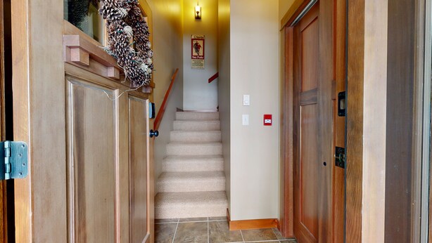 A wooden hallway with a staircase leading to a room. There is a pine cone wreath on the wall and a poster on the wall above the staircase. - Settler's Crossing Condo with Views of Tod Mountain! (Sun Peaks)