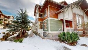 Ein verschneiter Weg führt zu einem mehrstöckigen Haus mit grüner Holzverkleidung und einer Holzterrasse.