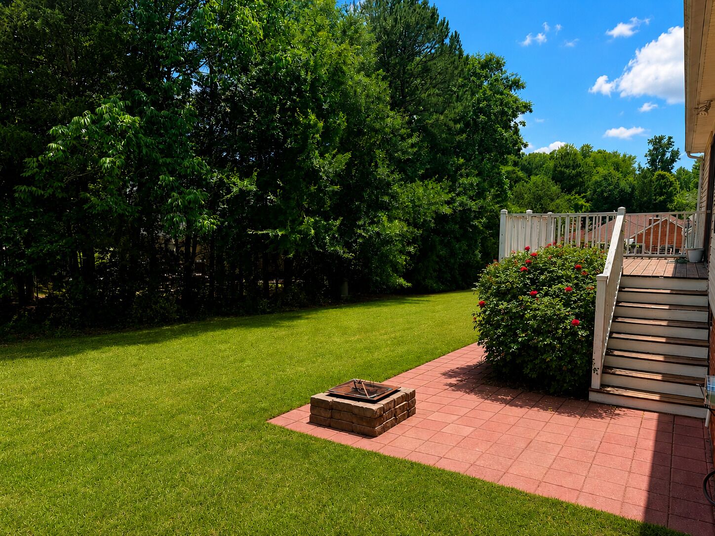 A well-maintained lawn, a brick fire pit, and a wooden deck with a white railing.