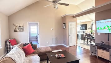 A spacious living room with a high ceiling, a ceiling fan, a sofa with cushions, a coffee table, and a television.