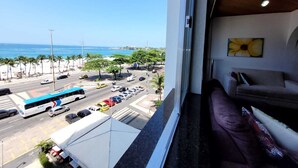 A view from a hotel room window overlooking a beach and a busy street with cars and a bus. - Copacabana Oceanfront • 3 Spacious Bedrooms • Incredible Ocean View (Rio de Janeiro)