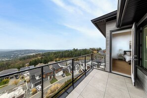 Uma varanda com vista para uma área residencial, um quarto com uma cama e uma mesa de cabeceira, e uma porta de vidro deslizante que dá para a varanda.