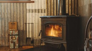 A rustic interior with a wood-burning stove, a vintage suitcase, and a metal ladder.