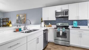 Une cuisine moderne avec des armoires blanches, des appareils en acier inoxydable et un pare-feu bleu.
